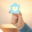A hand holds up a cutout of a home with a heart in it, representing the home care industry.