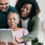 A daughter looks at a tablet with her older parents, representing technology and how ti can help with aging in place.