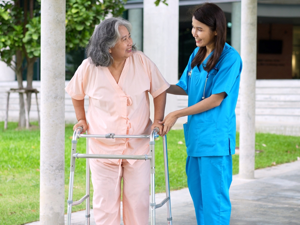 _Home Care in Northeast Philadelphia (1) Elderly woman using a walker assisted by a smiling caregiver in blue scrubs outdoors, representing compassionate home care in Northeast Philadelphia.