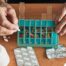 Older hands organize pills into a pill organizer, showing a great tool for managing medications.