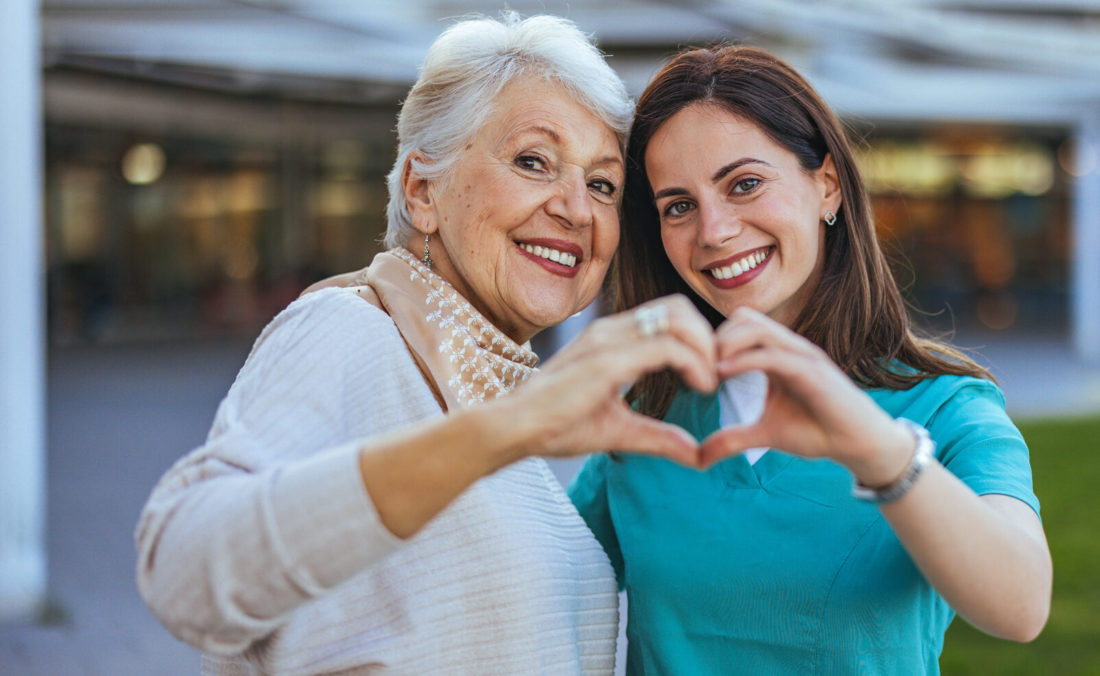 This image shows a cheerful female caregiver standing besides a senior woman The caregiver creates a heart with her hand and the seniors hand, symbolizing warm, personalized home care in Woodlyn.